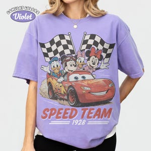 May include: A lilac Comfort Colors t-shirt with a graphic of Disney characters Mickey Mouse, Donald Duck, Daisy Duck, and Minnie Mouse in a race car. The car has the number 95 on it, and the text "SPEED TEAM 1928" is printed below the car.