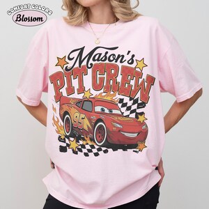 May include: Pink Comfort Colors t-shirt with a graphic of Lightning McQueen from the movie Cars. The design includes the text "Mason's PIT CREW" in red and yellow, with stars and a checkered flag.