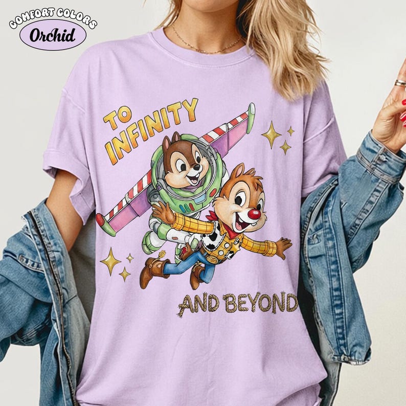 May include: A light purple Comfort Colors t-shirt with a graphic featuring Chip and Dale as Buzz Lightyear and Woody, with the text "TO INFINITY AND BEYOND". The shirt has short sleeves and a relaxed fit.