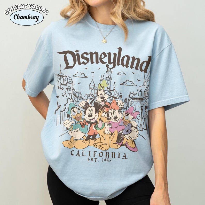 May include: Light blue t-shirt featuring a Disneyland graphic with Mickey Mouse, Minnie Mouse, Donald Duck, and other characters. The shirt includes the text "Disneyland California Est. 1955" in a vintage style.