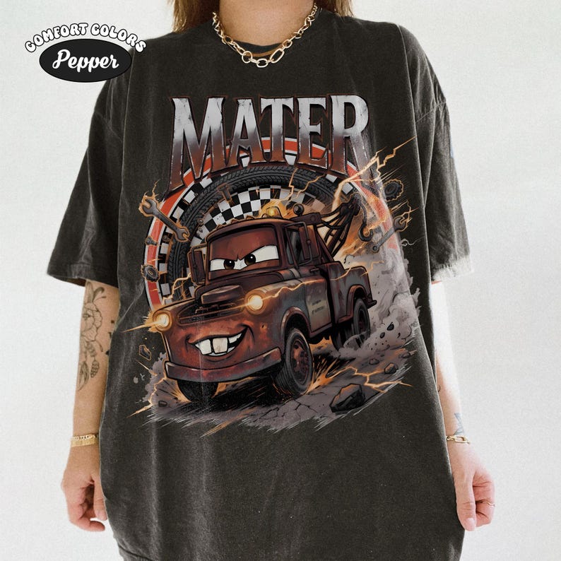 May include: Dark gray t-shirt featuring a cartoon image of Mater from the movie Cars. The word "MATER" is printed above the character. The shirt has a distressed look and the Comfort Colors Pepper logo is in the upper left corner.