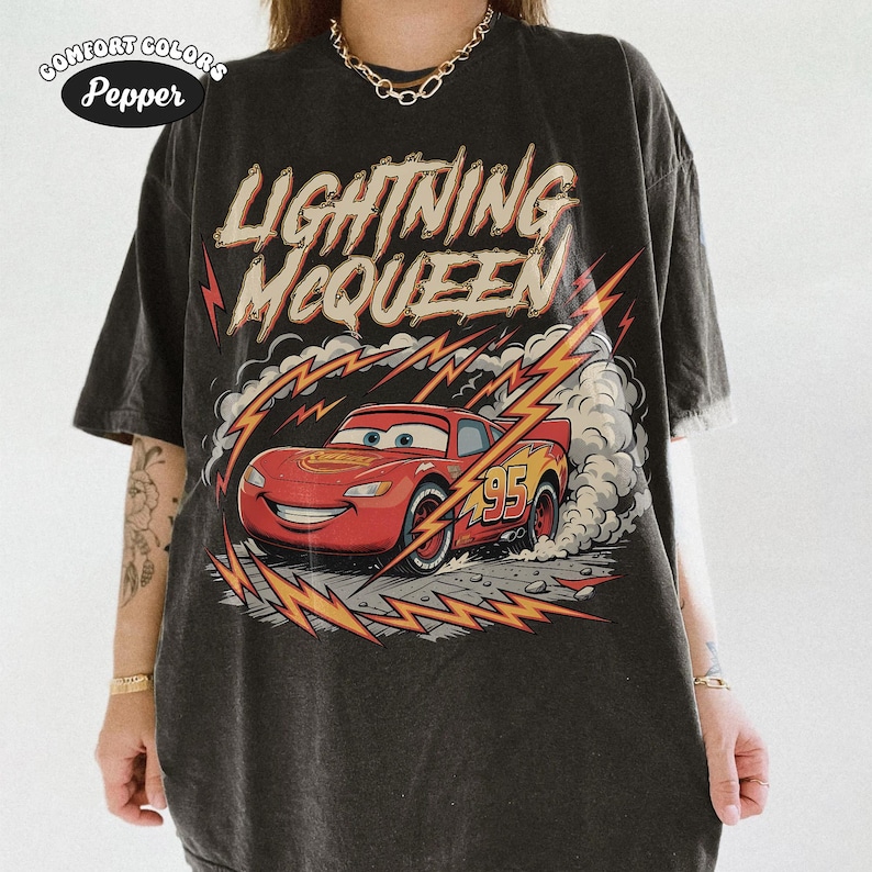 May include: Dark gray t-shirt featuring Lightning McQueen from the Cars movie. The design includes the text "LIGHTNING McQUEEN" above a red race car with the number 95. The shirt has a vintage, distressed look.