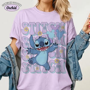 May include: A light purple short-sleeve t-shirt featuring a graphic of the blue character Stitch holding two balloons. The text STITCH is repeated in a wavy font behind the character, accented with small yellow and blue flowers and Mickey icons.