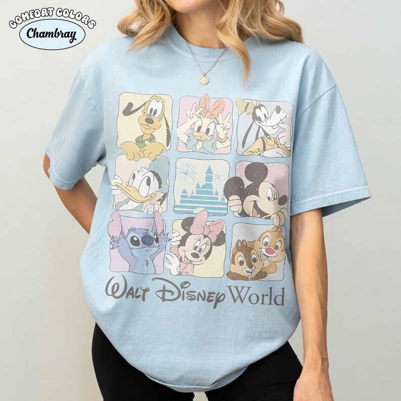Op de afbeelding: Een lichtblauw t-shirt met een raster van negen vierkanten met Disney-figuren waaronder Pluto, Katrien Duck, Goofy, Donald Duck, een kasteel, Mickey Mouse, Stitch, Minnie Mouse en Knabbel en Babbel, met de tekst Walt Disney World eronder.