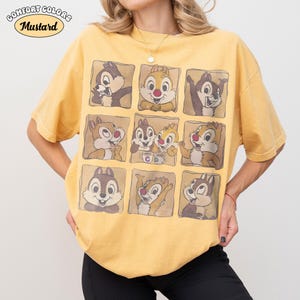 May include: Mustard-coloured t-shirt featuring a grid of cartoon chipmunks in various poses. The shirt has the words "Comfort Colors" and "Mustard" printed on it. The shirt is a relaxed fit.