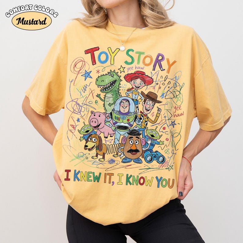 Puede incluir: Una camiseta de color amarillo mostaza con un gr&aacute;fico colorido de los personajes de Toy Story, incluyendo a Woody, Buzz Lightyear, Jessie, Rex, Hamm, Slinky Dog, Mr. Potato Head y alien&iacute;genas. El texto dice TOY STORY, yee haw e I KNEW IT, I KNOW YOU.