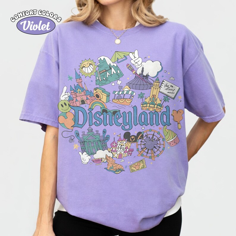 May include: A violet Comfort Colors t-shirt with a Disneyland graphic. The design features the castle, Matterhorn, and Mickey Mouse, with "Disneyland" in the centre. The shirt is a comfortable fit and a vibrant colour.