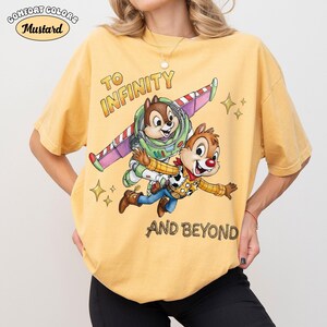 May include: Mustard-colored Comfort Colors t-shirt featuring Chip and Dale as Buzz Lightyear and Woody, with the text "TO INFINITY AND BEYOND." The shirt has a relaxed fit and a vintage aesthetic.