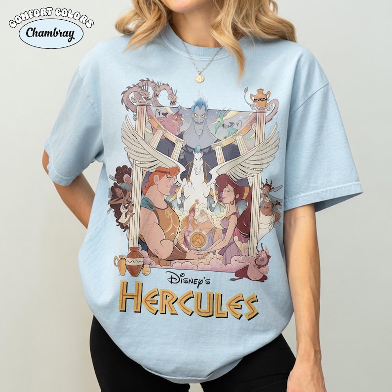 May include: Light blue Comfort Colors Chambray t-shirt featuring a graphic from Disney's Hercules. The design includes Hercules, Megara, Pegasus, Hades, and other characters. The text "Disney's Hercules" is in gold lettering.