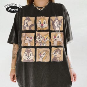 May include: Dark grey Comfort Colors t-shirt with a grid of Chip and Dale cartoon images. The cartoon characters are in various poses, set against a beige background. The shirt has the text "Comfort Colors Pepper" in a circular design.