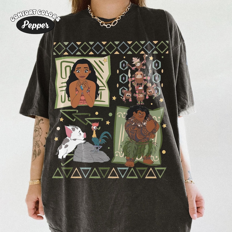 May include: A charcoal gray short-sleeve t-shirt featuring a graphic print with characters from the movie Moana, including Moana, Maui, Pua, Hei Hei, and Kakamora, arranged in panels with geometric borders and small star accents throughout the design.