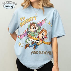 May include: Light blue Comfort Colors t-shirt featuring Chip and Dale as Buzz Lightyear and Woody from Toy Story, with the text "TO INFINITY AND BEYOND". The design includes a pink and white wing, stars, and the Comfort Colors and Chambray logos.
