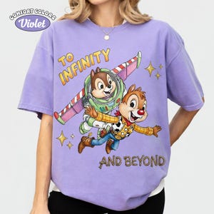 May include: Violet Comfort Colors t-shirt featuring a graphic of Chip and Dale as Buzz Lightyear and Woody from Toy Story. The phrase "TO INFINITY AND BEYOND" is printed in gold. The shirt has short sleeves.
