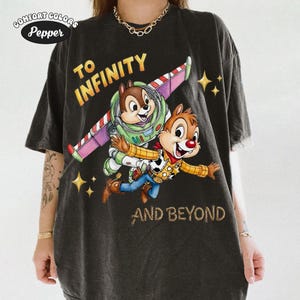 May include: Dark gray Comfort Colors t-shirt featuring Chip and Dale as Buzz Lightyear and Woody from Toy Story, with the text "TO INFINITY AND BEYOND". The design includes a colorful space-themed wing and star accents.