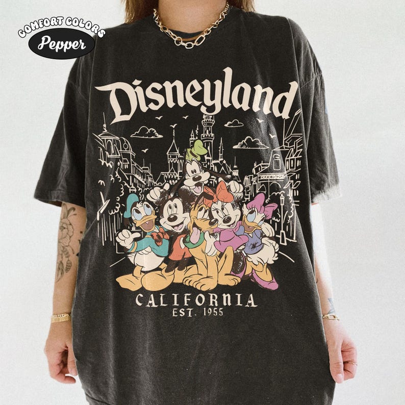 May include: Black t-shirt featuring the word "Disneyland" above a graphic of Disney characters, including Mickey Mouse, Donald Duck, and Goofy. The text "CALIFORNIA EST. 1955" is printed below the characters. The shirt has a vintage look.