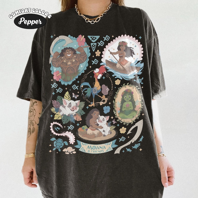May include: Black Comfort Colors t-shirt featuring a colorful graphic of characters from the animated film "Moana." The design includes images of Maui, Moana, Pua, Hei Hei, and other elements from the movie. The text "Moana & Friends" is also visible.