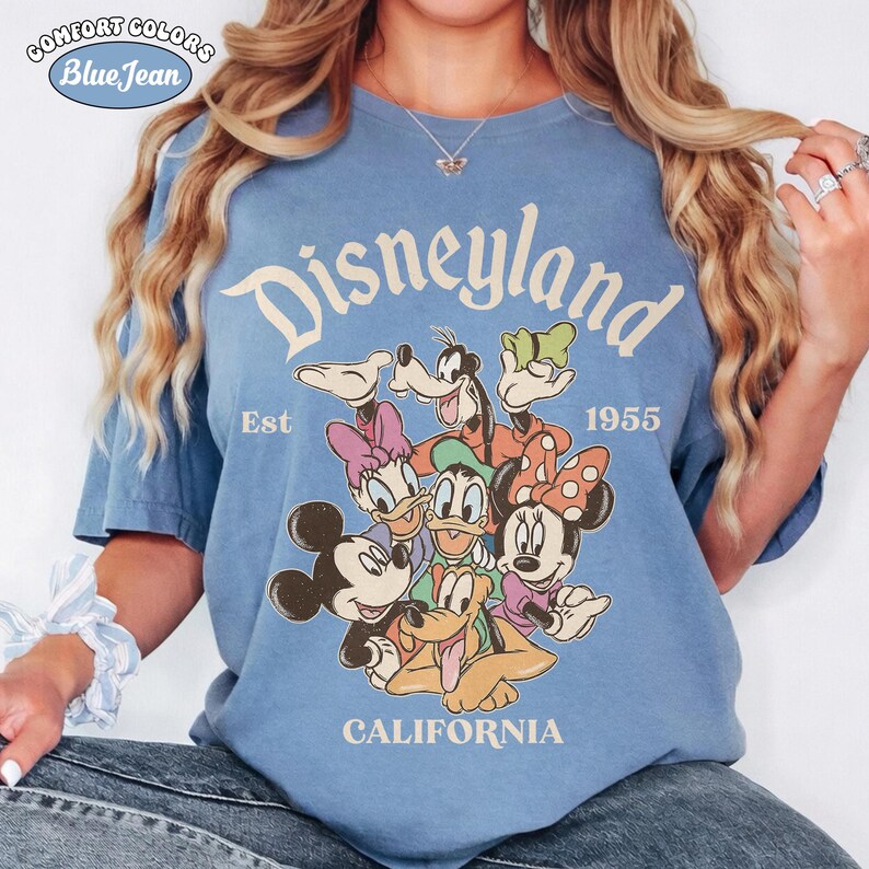 May include: Blue Comfort Colors t-shirt with a Disneyland graphic featuring Mickey Mouse, Minnie Mouse, Donald Duck, Daisy Duck, Goofy, and Pluto. The shirt includes the text "Disneyland", "Est 1955", and "California".