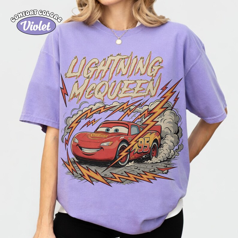 May include: A Comfort Colors violet t-shirt featuring Lightning McQueen from the Cars movie. The graphic shows the red race car with the number 95, surrounded by lightning bolts and the text "LIGHTNING McQUEEN".