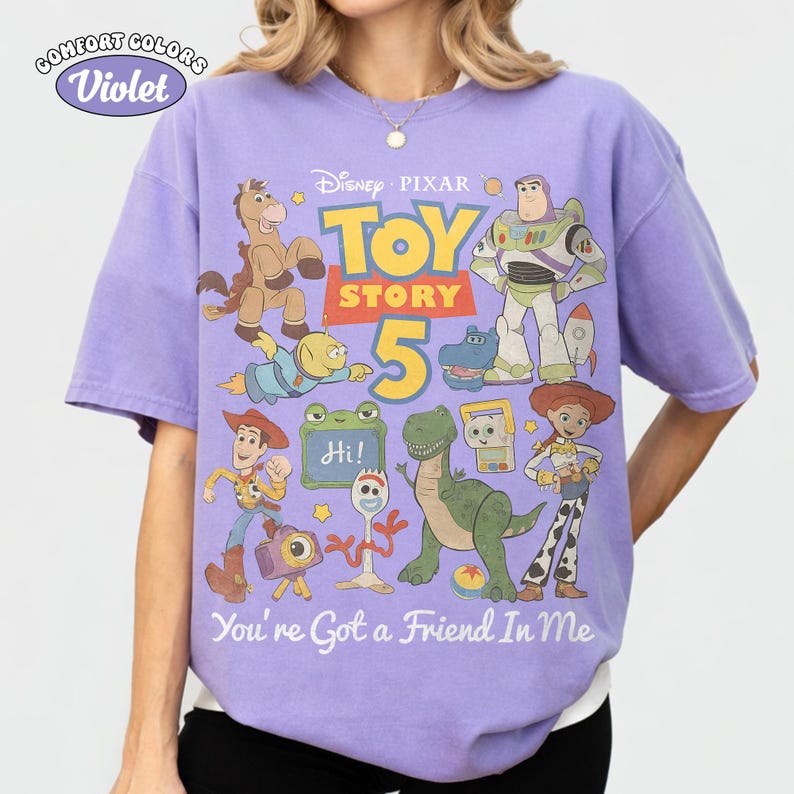 May include: A violet Comfort Colors t-shirt featuring a Toy Story 5 graphic. The design includes characters like Woody, Buzz Lightyear, and Jessie, with the text "You're Got a Friend In Me."