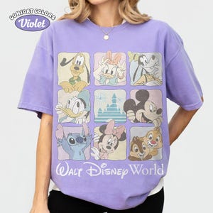 Op de afbeelding: Een violetkleurig t-shirt met korte mouwen en een raster van negen vierkanten met Disney-figuren zoals Pluto, Katrien Duck, Goofy, Donald Duck, een kasteel, Mickey Mouse, Stitch, Minnie Mouse en Knabbel en Babbel, met de tekst Walt Disney World.