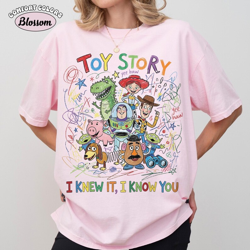 Puede incluir: Una camiseta rosa claro con un gr&aacute;fico colorido de los personajes de Toy Story, incluyendo a Woody, Buzz Lightyear, Rex, Jessie, Hamm, Mr. Potato Head, Slinky Dog y los Aliens. El dise&ntilde;o incluye garabatos, estrellas y el texto TOY STORY e I KNEW IT, I KNOW YOU.
