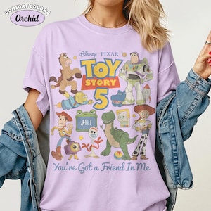 May include: A light purple Comfort Colors t-shirt featuring a graphic of characters from the Disney Pixar movie Toy Story 5. The design includes Woody, Buzz Lightyear, and the text "You're Got a Friend In Me."