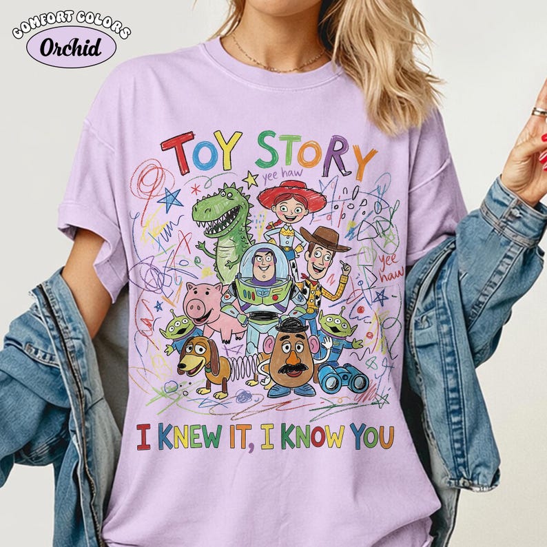 Puede incluir: Una camiseta de color morado claro con un gr&aacute;fico colorido de los personajes de Toy Story, incluyendo a Woody, Buzz Lightyear, Jessie, Rex, Hamm, Slinky Dog, Mr. Potato Head y alien&iacute;genas. El texto dice TOY STORY e I KNEW IT, I KNOW YOU.