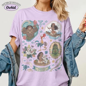 May include: A light purple t-shirt with a graphic featuring characters from the movie "Moana." The design includes illustrations of Maui, Moana, Pua, Hei Hei, and other elements. The text "Moana & Friends" is also present.