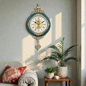 Könnte beinhalten: Eine verzierte Wanduhr mit einem türkis-goldenen Zifferblatt und römischen Ziffern. Die Uhr hat ein dekoratives Pendel und ist an einer hellgrauen Wand befestigt. Die Uhr ist im Vintage-Stil gehalten und verleiht jedem Raum einen Hauch von Eleganz.