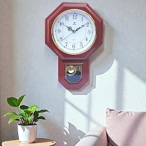 May include: A wooden wall clock with a white face, gold trim, and black hands. The clock has an octagonal shape and a pendulum. The clock is hanging on a light-colored wall.