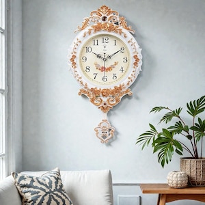 May include: A white and gold ornate wall clock with a cream-colored face. The clock features Roman numerals, floral accents, and a decorative pendulum. The clock is mounted on a light blue wall, with a plant in a woven pot in the background.