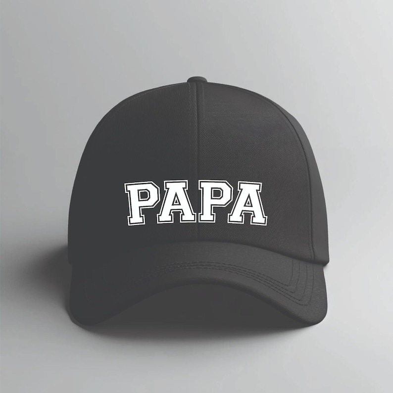 May include: Black baseball cap with the word "PAPA" in white, block letters across the front. The hat has a curved brim and a rounded crown. The text is outlined in a contrasting color.