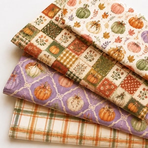 May include: Three folded pieces of fabric featuring autumn themes. The top layer has pumpkins and leaves on cream. The middle layer shows a patchwork grid of pumpkins and floral patterns. The bottom layer displays a plaid pattern in orange and green.