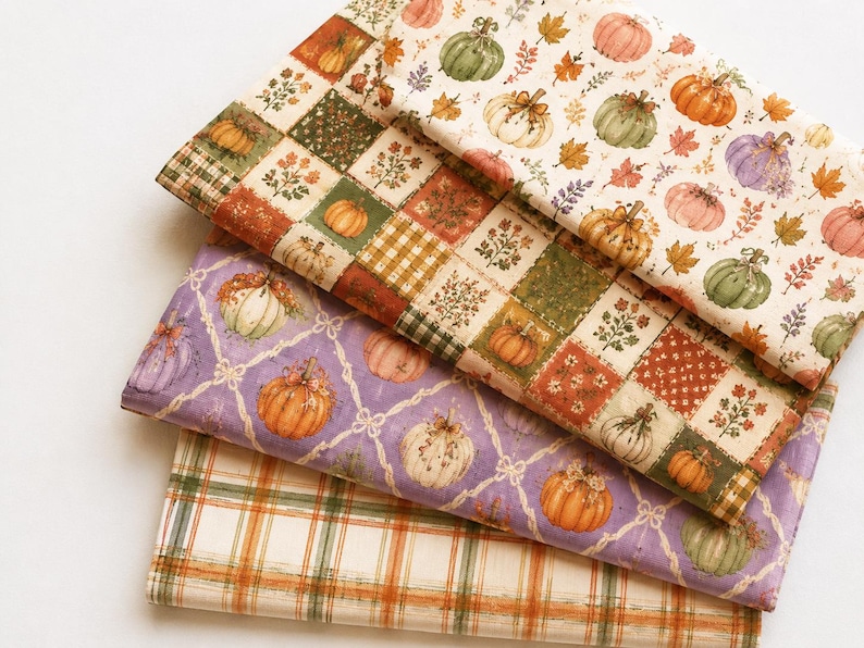 May include: Three folded pieces of fabric featuring autumn themes. The top layer has pumpkins and leaves on cream. The middle layer shows a patchwork grid of pumpkins and floral patterns. The bottom layer displays a plaid pattern in orange and green.