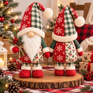 Puede incluir: Dos figuras de gnomos de peluche con sombreros altos de cuadros rojos y verdes y patrones de copos de nieve, rematados con pompones blancos. Tienen largas barbas blancas, manoplas rojas y botas rojas de lunares. Un gnomo sostiene ramas.