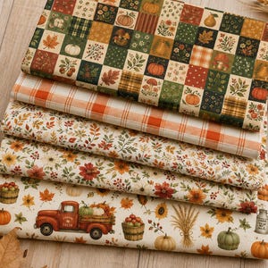 May include: A stack of five folded fabric pieces featuring autumn-themed patterns. Designs include a patchwork grid of pumpkins and leaves, orange plaid, small colorful foliage, large floral prints, and a red truck carrying pumpkins and apples.