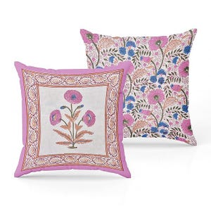 May include: Two decorative throw pillows. One pillow features a floral design with pink flowers and a white background, framed by a pink border. The other pillow has a repeating floral pattern with pink and blue flowers.