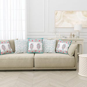 May include: A beige sofa with four decorative throw pillows. Two pillows feature a floral design with red and pink flowers, while the other two have a light blue leaf pattern. The pillows have a turquoise border.