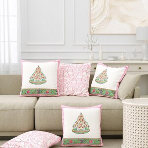 May include: A collection of decorative throw pillows in a living room setting. The pillows feature a white background with colorful floral designs and pink trim. One pillow has a pink pattern. The pillows are arranged on a beige sofa and on the floor.