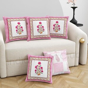 May include: Five decorative throw pillows with floral designs. Four pillows feature a white center with a pink floral print, framed by a pink and white striped border. The fifth pillow has a pink and white geometric pattern.