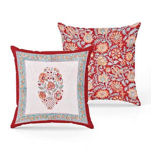 May include: Two square throw pillows. One pillow has a white center with a floral design in a vase, framed by a teal and orange border, and a red border. The other pillow has a red background with a floral pattern in orange, teal, and white.