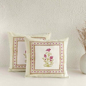 May include: Two square throw pillows with a floral design. The pillows have a white center with a pink floral print and a striped border in green and white. The outer border is a repeating pink floral pattern.