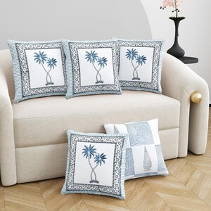 May include: Five square throw pillows with blue and white designs. Four pillows feature a white center with a blue palm tree illustration, framed by a blue patterned border. The fifth pillow has a geometric design.