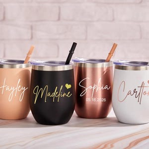 Puede incluir: Cuatro vasos de acero inoxidable con tapas y pajitas. El primero es color melocotón con el nombre Hayley, el segundo es negro con el nombre Madeline y un corazón, el tercero es oro rosa con el nombre Sophia y fecha 05.16.2026, y el cuarto es blanco con el nombre Carlton y un corazón.