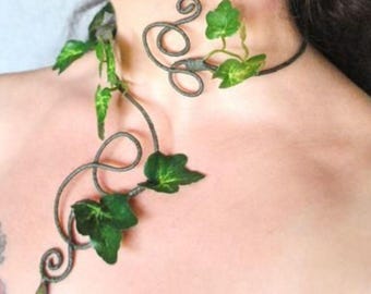 May include: A dark metal choker necklace featuring a spiraling wire design adorned with green ivy leaves. The necklace extends downward in a curved, vine-like shape, ending with a small, metallic gold-toned teardrop accent at the bottom tip.