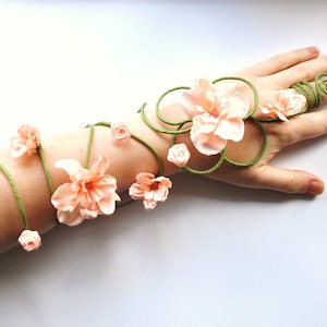 May include: A delicate floral arm cuff made with peach-colored paper flowers and green paper vines. The cuff wraps around the wrist and up the forearm, with the vines forming a spiral design.