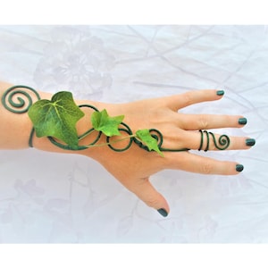 May include: A dark green wire hand bracelet featuring a series of connected metal spirals and three realistic green ivy leaves. The wire structure extends from a wrist cuff across the back of the hand to a single ring worn on the middle finger.