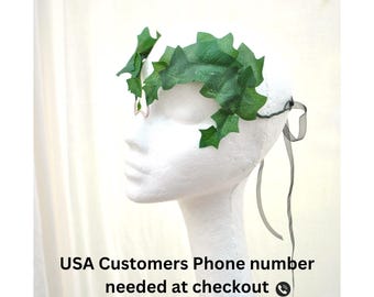 May include: A decorative headpiece featuring green ivy leaves. The leaves are arranged in a crown shape and attached to a white base. Black ribbons hang from the base. The text "USA Customers Phone number needed at checkout" is at the bottom.
