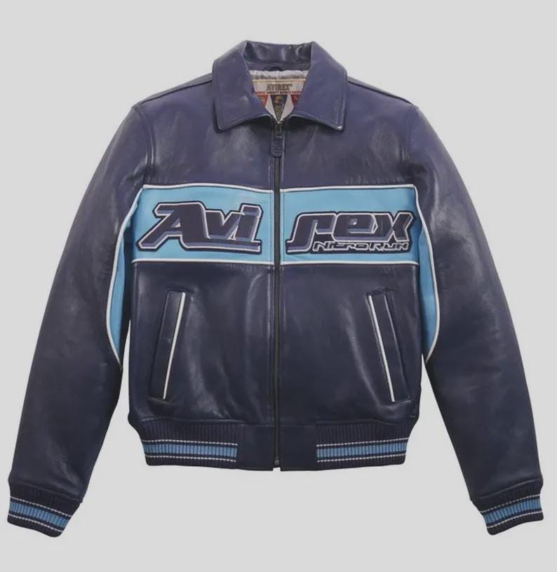 K&ouml;nnte beinhalten: Marineblaue Lederjacke mit hellblauem Streifen auf der Brust, mit dem Text "Avi Rex" in Wei&szlig;. Die Jacke hat einen Kragen, einen Rei&szlig;verschluss und gerippte B&uuml;ndchen und Saum. Klassischer Bomber-Stil.