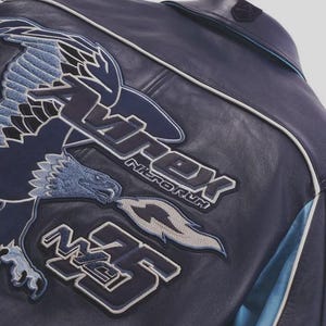 K&ouml;nnte beinhalten: Marineblaue Lederjacke mit gesticktem Adler und Textdetails. Die Jacke hat ein gro&szlig;es Adlerdesign in Blau- und Wei&szlig;t&ouml;nen sowie den Text "Apex Nitroforum" und die Zahl "35". Wei&szlig;e und hellblaue Akzente sind sichtbar.